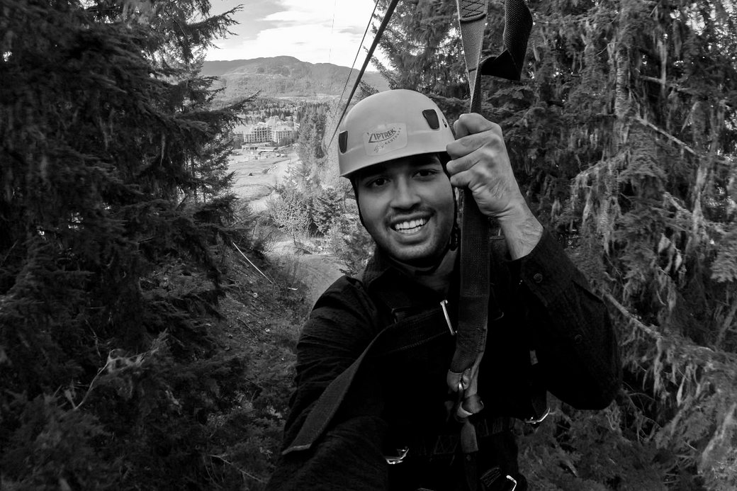 Nasmaan on a zipline high above the Whistler valley, in a helmet and harness, grinning at the camera.
